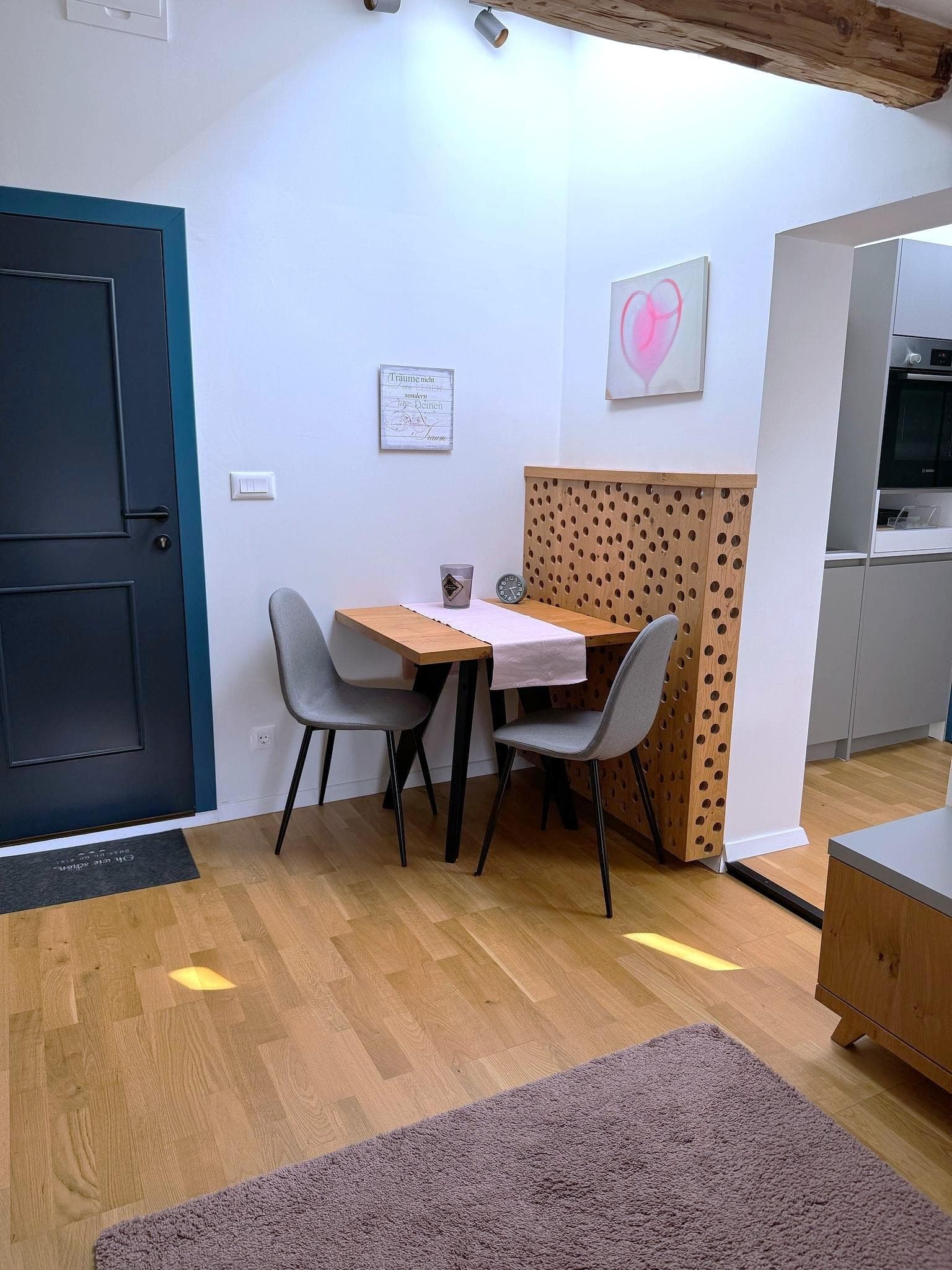 Apartments Kapelln · Kuschellounge - A charming bedroom with a bed adorned with heart-themed pillows and bedding. A white knitted blanket is folded into a heart shape on the bed. The room features a wooden ceiling with skylights, creating a warm and cozy atmosphere.